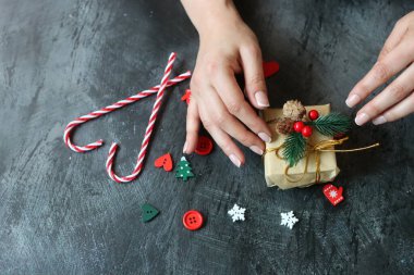 Güzel manikürlü kadın elleri koyu arkaplanda Noel hediyesi taşıyor.