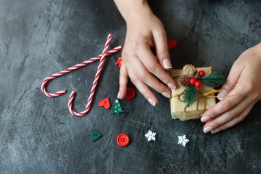 Güzel manikürlü kadın elleri koyu arkaplanda Noel hediyesi taşıyor.