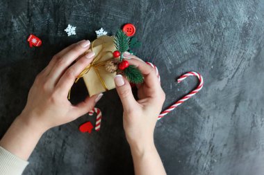 Hediye paketleyen kadın ellerinin yakın çekimi. Koyu gri arkaplan ve metin için boşluk. Noel kutlaması kavramı