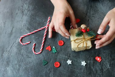 Hediye paketleyen kadın ellerinin yakın çekimi. Koyu gri arkaplan ve metin için boşluk. Noel kutlaması kavramı