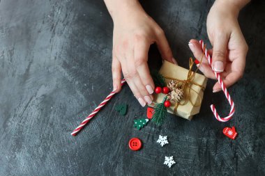 Güzel manikürlü kadın elleri koyu arkaplanda Noel hediyesi taşıyor.