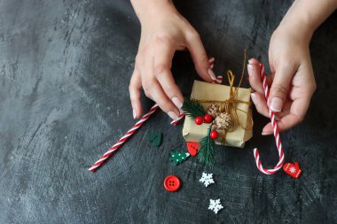 Hediye paketleyen kadın ellerinin yakın çekimi. Koyu gri arkaplan ve metin için boşluk. Noel kutlaması kavramı