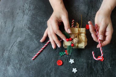 Hediye paketleyen kadın ellerinin yakın çekimi. Koyu gri arkaplan ve metin için boşluk. Noel kutlaması kavramı