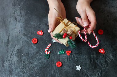Güzel manikürlü kadın elleri koyu arkaplanda Noel hediyesi taşıyor.