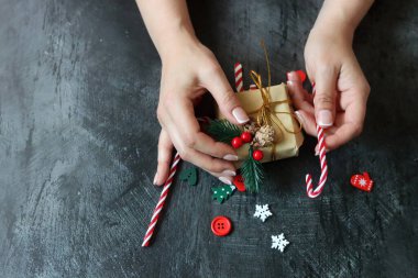 Güzel manikürlü kadın elleri koyu arkaplanda Noel hediyesi taşıyor.