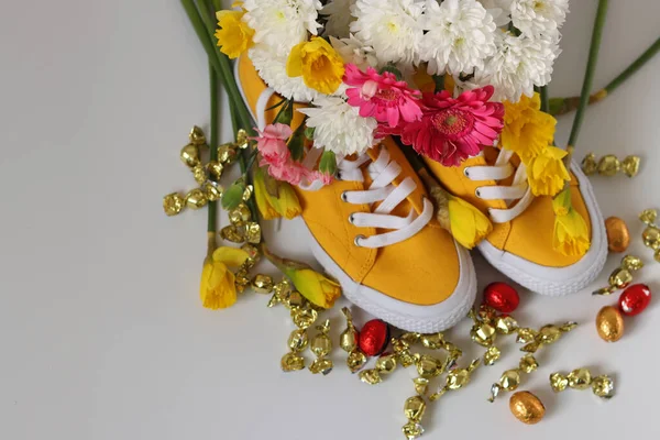 Sarı nergisli sarı spor ayakkabılar ve pembe arka planda çikolatalı yumurtalar. Paskalya kutlaması kavramı.