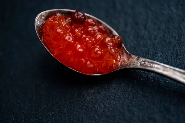 Siyah arka planda kırmızı havyarla dolu gümüş kaşık. Çok değerli bir ürün, nefis bir tadı, sağlıklı özellikleri ve yüksek maliyeti var..