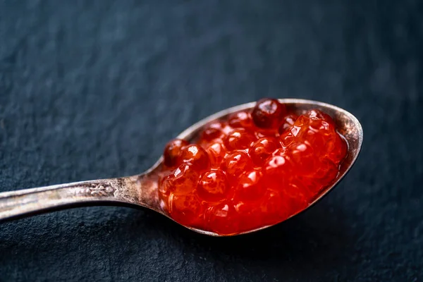 Siyah arka planda gümüş kaşıkta kırmızı havyar. Çok değerli bir ürün, nefis bir tadı, sağlıklı özellikleri ve yüksek maliyeti var..