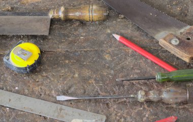 Diğer el aletleri eski, gri ahşap zemine yerleştirilmiş, el işi için hazırlanmış. Yukarıdan çekilen fotoğraflar, sahne çubuğu, sarı mezura, kırmızı ahşap kalem, tornavida, çelik pense, marangoz masası arka planı..