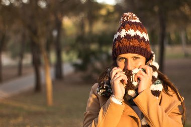 Sonbahar-kış mevsiminde ormanda yün şapka, eşarp ve kahverengi ceket giyen genç bir kadın..