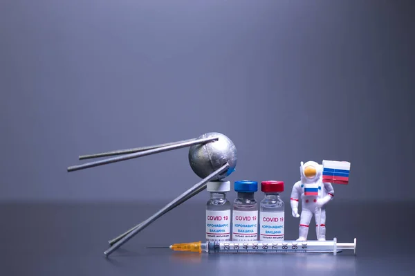 Bir grup Rus, Covid 19 virüsüne karşı şırıngalı ve küçük astronotla bilinen bir Rus uydusunun adını taşıyor. Gri arkaplan ve odak dışı.