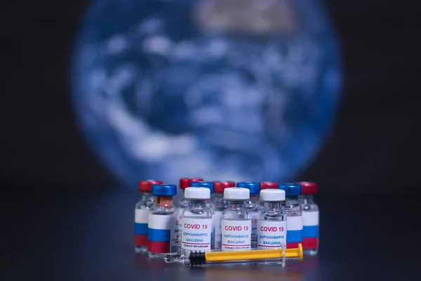 Covid 19 virüsü ve şırıngaya karşı bir grup Rus aşısı. Dünya gezegeninin arka planında ve odak dışı. Etiket metni, sadece korona virüsü enjeksiyonu.