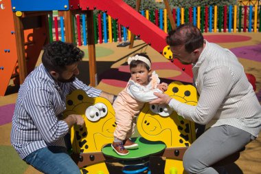 Eşcinsel evli çift, oyun alanında kızlarıyla çok mutlu bir şekilde oynuyorlar. Aile çeşitliliği.