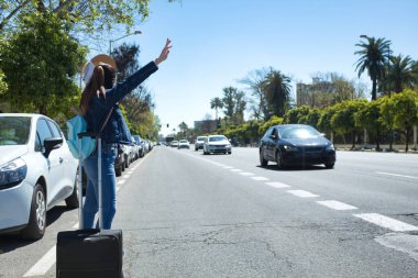 Genç ve güzel Asyalı turist tatil gezisi sırasında şehir caddesinde bir taksi durduruyor..
