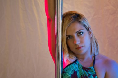 Kadın striptizcinin portresi. Kenarlarında mavi ve kırmızı ışıklar olan şehvetli bir şekilde direğe tutunuyor..