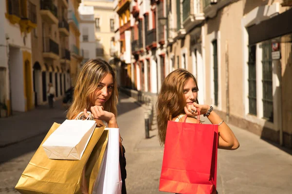 Duas Jovens Mulheres Com Sacos Compras Nos Ombros Olhando Para — Fotografia de Stock