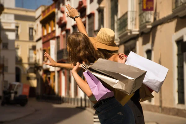 Duas Jovens Mulheres Com Sacos Compras Nos Ombros Levantando Braços — Fotografia de Stock