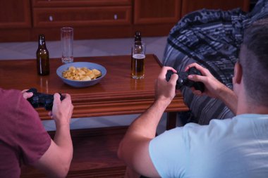 İki adam. Biri olgun, biri de kanepede oturmuş video oyunu oynayan bir genç..