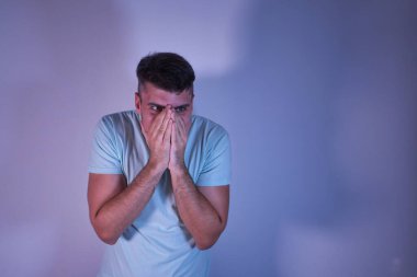 Genç İspanyol bir adam elleri ve burnu ve ağzı kapalı, beyaz bir arka planda şaşkın ve şaşkın bakıyor.
