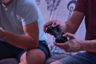 Bir arkadaşla oynarken elinde bir video konsol kumandası tutan adamın ayrıntıları.