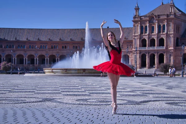 ヒスパニックな大人の女性古典的なバレエダンサーで 赤いチュチュで人物をやっています広場の真ん中で晴れた日に噴水を背景に — ストック写真