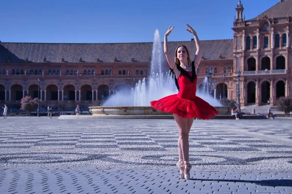 ヒスパニックな大人の女性古典的なバレエダンサーで 赤いチュチュで人物をやっています広場の真ん中で晴れた日に噴水を背景に — ストック写真