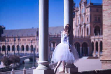 Yetişkin kadın İspanyol klasik balerin, iki taş sütun arasında beyaz etekli figürler yapıyor..