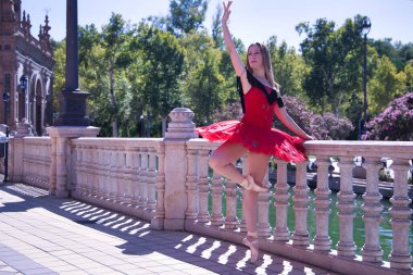 Kırmızı etekli İspanyol kadın klasik balerin güneşli bir günde plazanın ortasında taş korkulukların yanında figürler yapıyor..