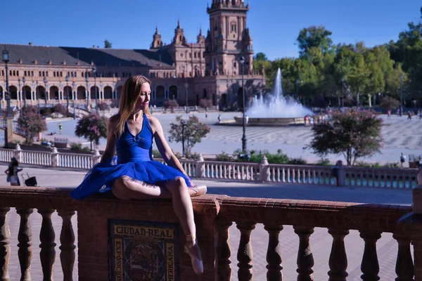 Yetişkin kadın klasik bale dansçısı, mavi etekli, kare bir balkonun üzerinde oturuyor..