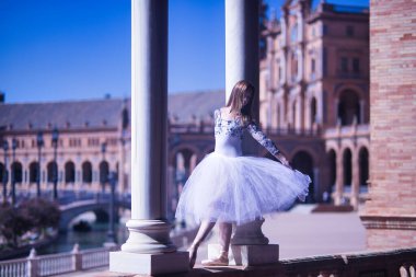 Yetişkin kadın İspanyol klasik balerin, iki taş sütun arasında beyaz etekli figürler yapıyor..