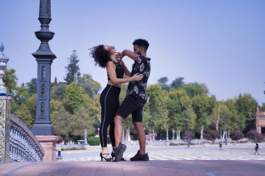 Çok ırklı genç bir çift, dışarıda şehvetle dans ederken figürler yapıyor..