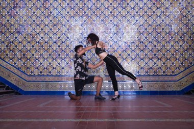 Çok ırklı genç bir çift, güzel fayanslı bir duvarın yanında şehvetli bir şekilde dans ederken figürler yapıyor..