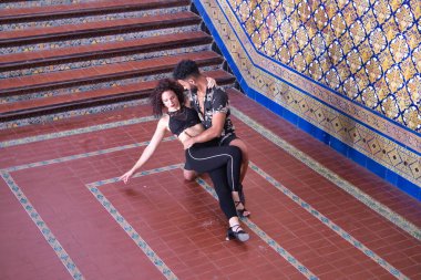 Çok ırklı genç bir çift, güzel fayanslı bir duvarın yanında şehvetli bir şekilde dans ederken figürler yapıyor..