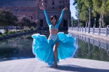 Orta yaşlı, turkuaz elmaslı İspanyol kadın, göbek dansı yaparken elbisesini kaldırıyor. Göbek dansı konsepti.