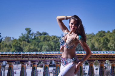 Orta yaşlı İspanyol bir kadın, elmaslı beyaz bir elbise giyiyor, göbek dansı yapıyor, fayans korkuluklarının yanında dans ederken figürler yapıyor. Göbek dansı konsepti.