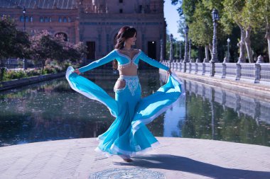 Orta yaşlı, turkuaz elbiseli, yapay elmasları olan, göbek dansı yaparken elbisesini tutan İspanyol bir kadın. Göbek dansı konsepti.