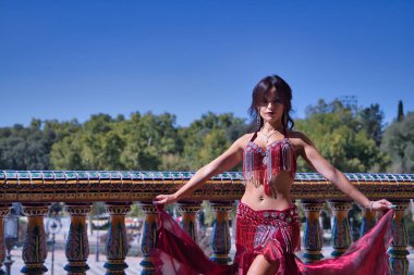 Orta yaşlı İspanyol kadın, kırmızı elbiseli ve yapay elmaslı, göbek dansı yapıyor, fayans korkuluklarının yanında dans ederken figürler yapıyor. Göbek dansı konsepti.