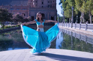 Orta yaşlı, turkuaz elmaslı İspanyol kadın, göbek dansı yaparken elbisesini kaldırıyor. Göbek dansı konsepti.