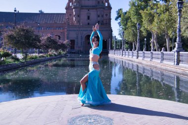 Orta yaşlı, turkuaz elbiseli, yapay elmaslı İspanyol kadın göbek dansı figürleri yapıyor. Göbek dansı konsepti.