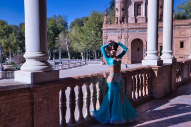 Orta yaşlı İspanyol kadın, turkuaz kostüm ve yapay elmaslar giyiyor, göbek dansı için, taş bir balerin yanında dans ederken figürler yapıyor. Göbek dansı konsepti.