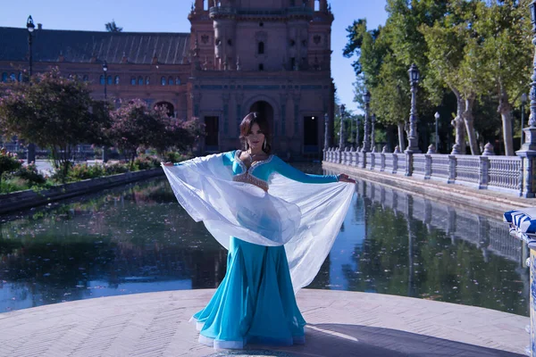 Orta yaşlı, turkuaz elbiseli, yapay elmaslı İspanyol kadın, beyaz peçeli göbek dansı. Göbek dansı konsepti.