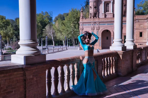 Orta yaşlı İspanyol kadın, turkuaz kostüm ve yapay elmaslar giyiyor, göbek dansı için, taş bir balerin yanında dans ederken figürler yapıyor. Göbek dansı konsepti.