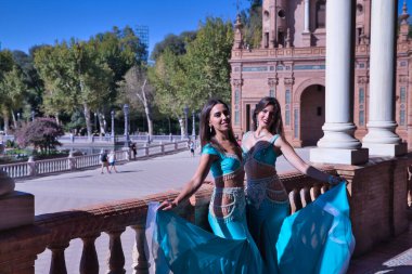 Orta yaşlı İspanyol kadınlar, turkuaz kostümler ve yapay elmaslar giyiyorlar, göbek dansına gidiyorlar, taş bir korkuluğun yanında dans ederken figürler yapıyorlar. Göbek dansı konsepti.