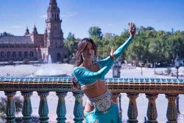 Orta yaşlı İspanyol kadın, turkuaz elbise ve elmaslar giyiyor, göbek dansı için, fayansların yanında dans ederken figürler yapıyor. Göbek dansı konsepti.