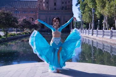 Orta yaşlı, turkuaz elmaslı İspanyol kadın, göbek dansı yaparken elbisesini kaldırıyor. Göbek dansı konsepti.