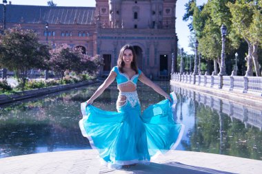 Orta yaşlı, turkuaz elmaslı İspanyol kadın, göbek dansı yaparken elbisesini kaldırıyor. Göbek dansı konsepti.