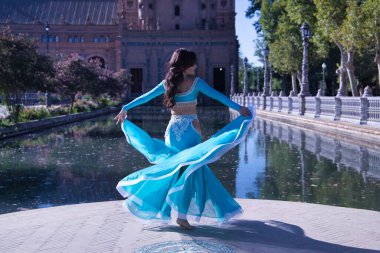 Orta yaşlı, turkuaz elbiseli, yapay elmasları olan, göbek dansı yaparken elbisesini tutan İspanyol bir kadın. Göbek dansı konsepti.