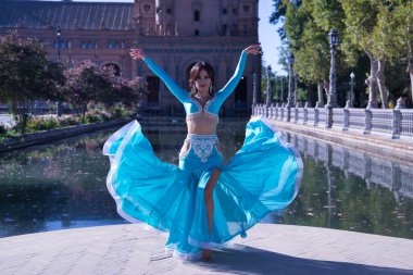 Orta yaşlı, turkuaz elmaslı İspanyol kadın, göbek dansı yaparken elbisesini kaldırıyor. Göbek dansı konsepti.