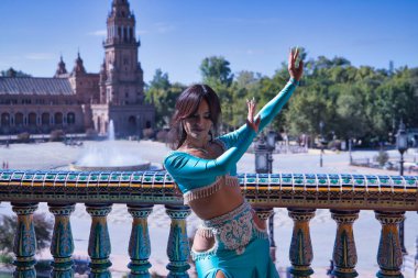 Orta yaşlı İspanyol kadın, turkuaz elbise ve elmaslar giyiyor, göbek dansı için, fayansların yanında dans ederken figürler yapıyor. Göbek dansı konsepti.