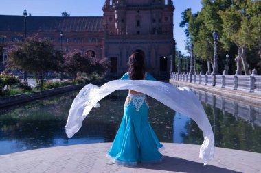Orta yaşlı, turkuaz elbiseli, yapay elmaslı İspanyol kadın, beyaz peçeli göbek dansı. Göbek dansı konsepti.